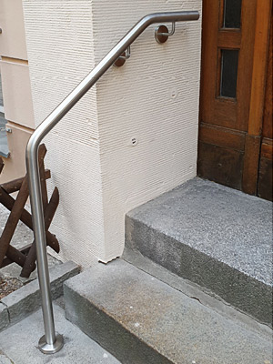 Edelstahl Handlauf gebogen mit einer Befestigung an der Wand und vor der Treppe